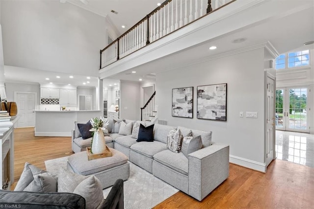 living room featuring baseboards, ornamental molding, a high ceiling, stairs, and light wood-style floors