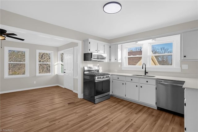 kitchen with appliances with stainless steel finishes, sink, white cabinets, ceiling fan, and light wood-type flooring