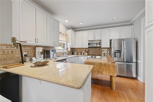 kitchen with a sink, a peninsula, stainless steel appliances, crown molding, and white cabinetry