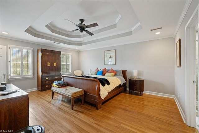 bedroom with visible vents, crown molding, a raised ceiling, baseboards, and light wood-style floors