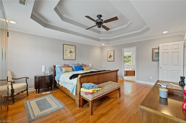 bedroom with a tray ceiling, crown molding, light wood-type flooring, ensuite bathroom, and baseboards