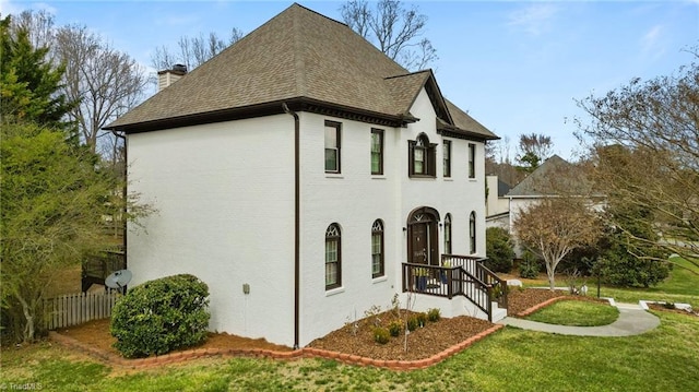 view of property exterior featuring roof with shingles, fence, brick siding, a chimney, and a lawn