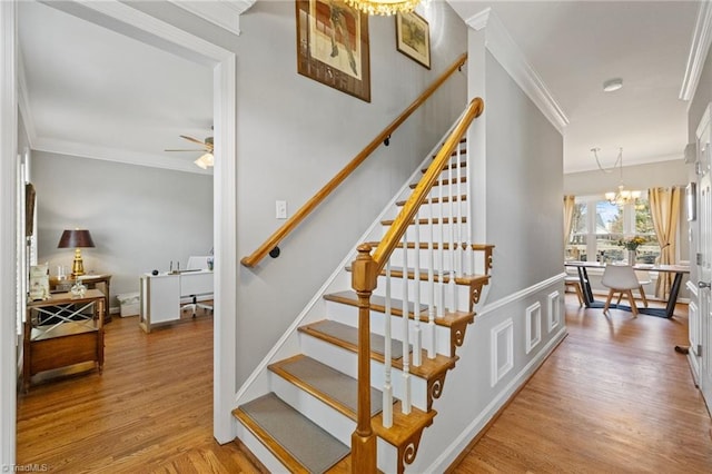stairway with crown molding, ceiling fan with notable chandelier, and wood finished floors