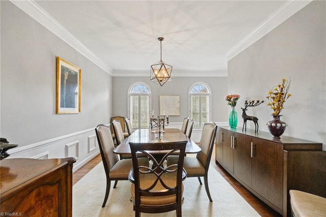 dining room with light wood-type flooring, wainscoting, and crown molding