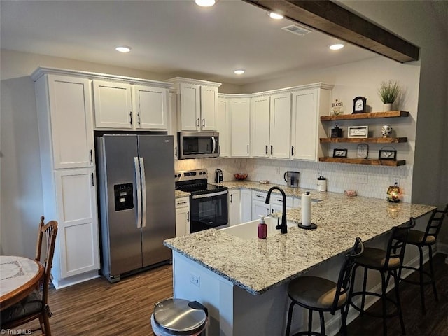 kitchen featuring a kitchen breakfast bar, kitchen peninsula, decorative backsplash, white cabinets, and appliances with stainless steel finishes