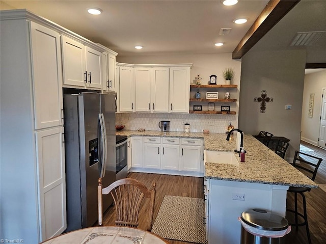 kitchen with a kitchen bar, stainless steel refrigerator with ice dispenser, light stone counters, sink, and white cabinetry