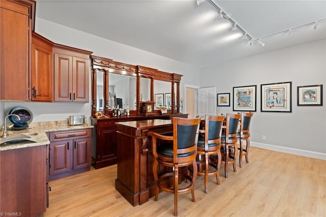 bar featuring rail lighting, light hardwood / wood-style floors, sink, and light stone counters