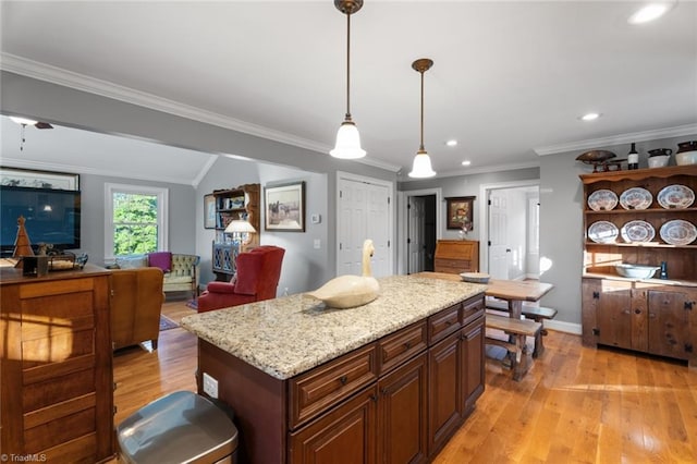 kitchen with a kitchen island, hanging light fixtures, ornamental molding, light stone counters, and light hardwood / wood-style floors