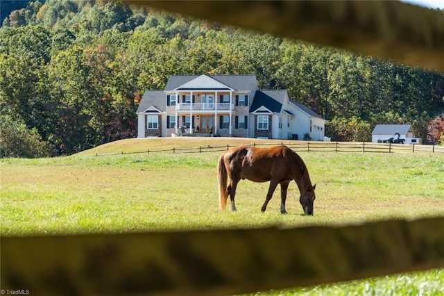 exterior space with a rural view, a balcony, and a front lawn