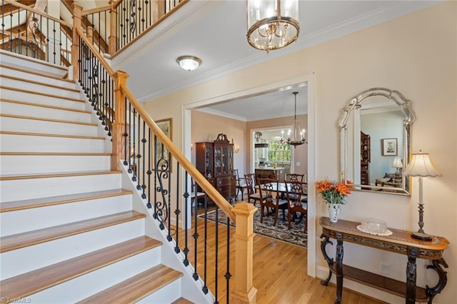 stairs featuring hardwood / wood-style flooring, ornamental molding, and a chandelier