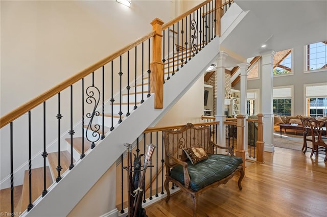 stairway featuring hardwood / wood-style flooring, a large fireplace, a high ceiling, and decorative columns