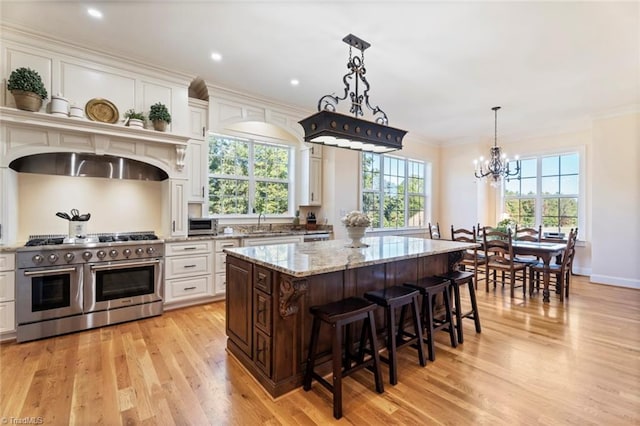 kitchen with light wood-type flooring, range with two ovens, a center island, white cabinetry, and a chandelier