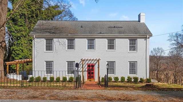 colonial house featuring a chimney, fence private yard, a pergola, and brick siding