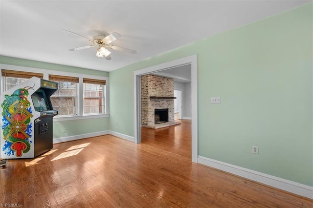 interior space with a fireplace, wood finished floors, baseboards, and ceiling fan