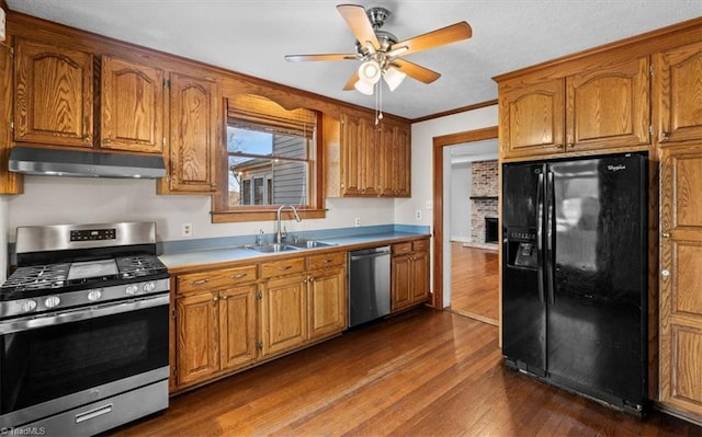 kitchen with brown cabinets, under cabinet range hood, a sink, appliances with stainless steel finishes, and dark wood-style flooring