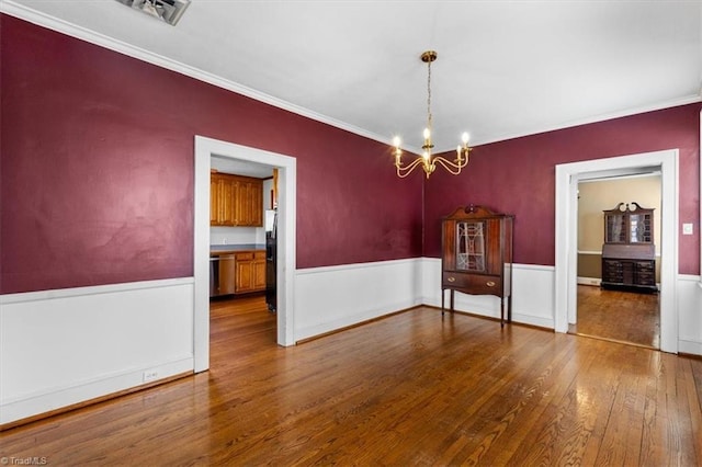 unfurnished dining area with visible vents, wainscoting, an inviting chandelier, and wood-type flooring