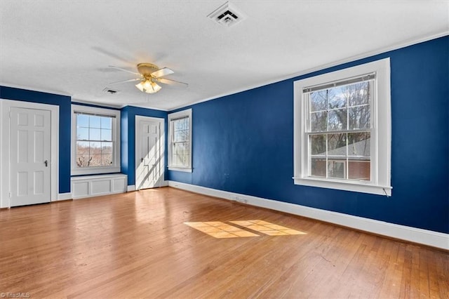 empty room featuring visible vents, crown molding, baseboards, wood finished floors, and a ceiling fan