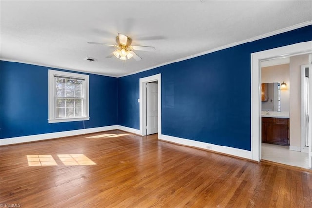 empty room featuring wood finished floors, crown molding, a ceiling fan, and baseboards