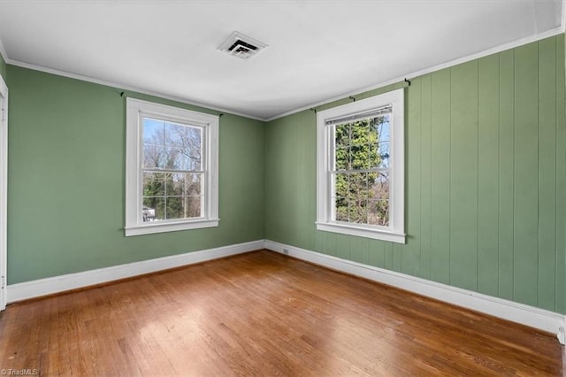 empty room featuring ornamental molding, wood finished floors, visible vents, and baseboards