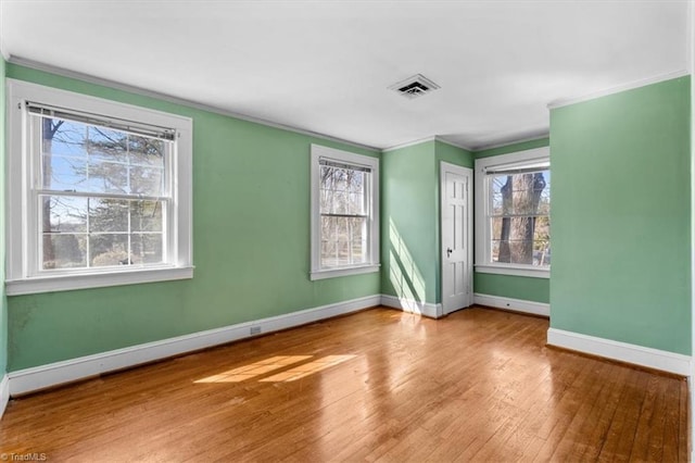 empty room featuring a wealth of natural light, visible vents, wood finished floors, and ornamental molding