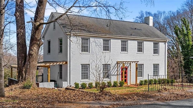 colonial inspired home featuring brick siding, a chimney, and fence