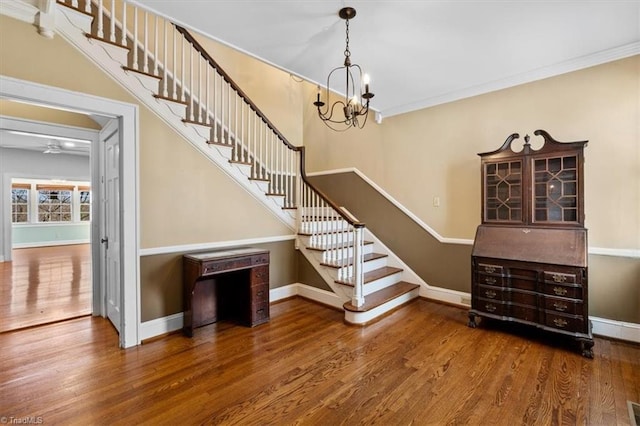 stairway featuring a chandelier, crown molding, baseboards, and wood finished floors