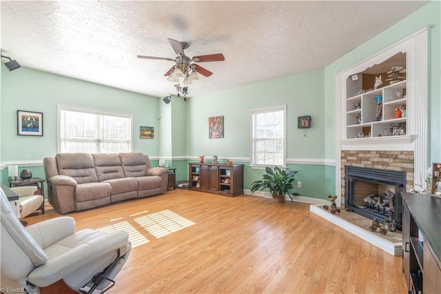 living room with a stone fireplace, ceiling fan, a textured ceiling, and hardwood / wood-style flooring