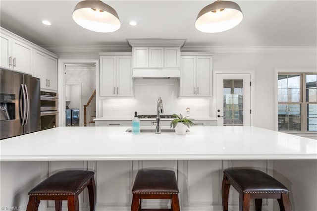 kitchen featuring crown molding, a breakfast bar area, stainless steel appliances, white cabinets, and a center island with sink