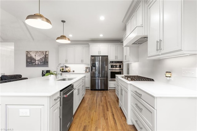 kitchen featuring appliances with stainless steel finishes, white cabinetry, sink, hanging light fixtures, and a center island with sink