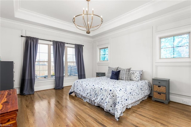 bedroom with crown molding, wood-type flooring, a raised ceiling, and a notable chandelier