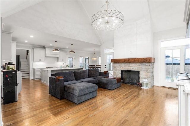 living room with high vaulted ceiling, a fireplace, sink, a notable chandelier, and light wood-type flooring