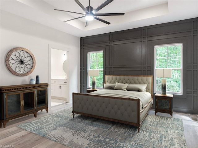 bedroom with ensuite bathroom, a tray ceiling, multiple windows, and light wood-style floors