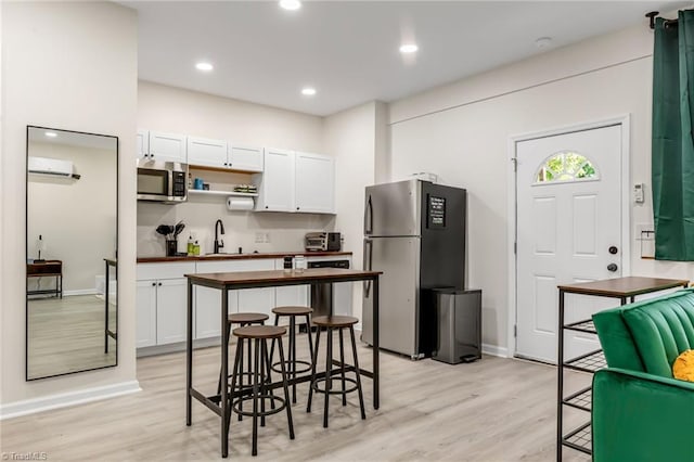 kitchen featuring a wall unit AC, a sink, white cabinets, light wood-style floors, and appliances with stainless steel finishes