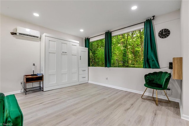 living area with an AC wall unit, light wood-style floors, and baseboards