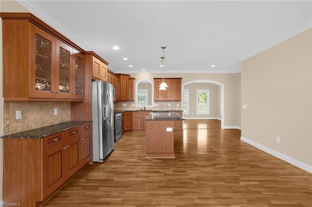 kitchen featuring hanging light fixtures, stainless steel appliances, ornamental molding, a kitchen island, and dark stone counters