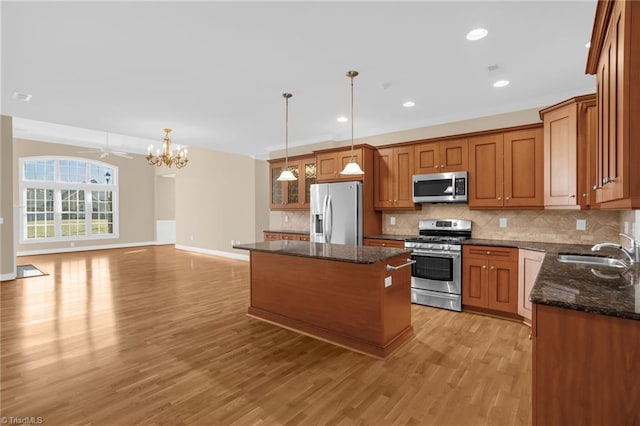 kitchen with sink, hanging light fixtures, dark stone countertops, appliances with stainless steel finishes, and a kitchen island