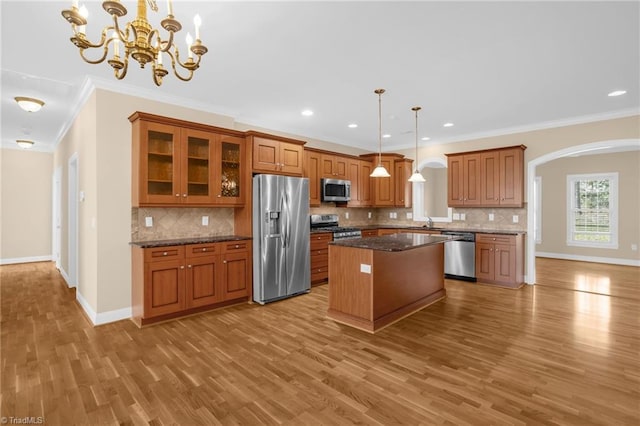 kitchen with dark stone countertops, stainless steel appliances, a center island, decorative light fixtures, and light wood-type flooring