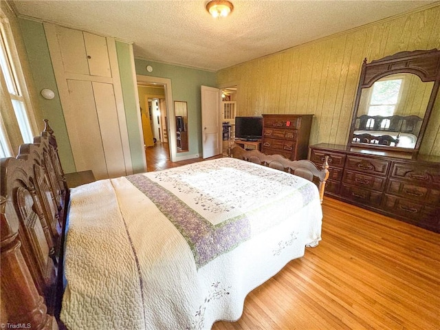 bedroom featuring wood walls, a textured ceiling, and light hardwood / wood-style flooring