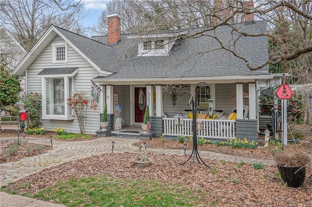 view of front facade featuring a chimney, a porch, and a shingled roof