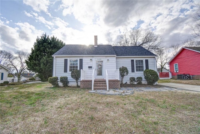 view of front of home with central AC, a chimney, a front lawn, and a shingled roof