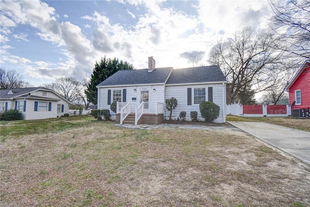 view of front of home featuring fence, roof with shingles, a chimney, a front lawn, and central air condition unit