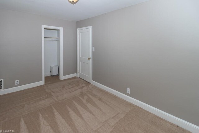 unfurnished bedroom with light colored carpet and a closet