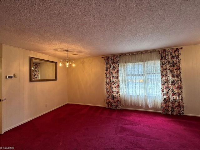 spare room featuring a textured ceiling, an inviting chandelier, and carpet