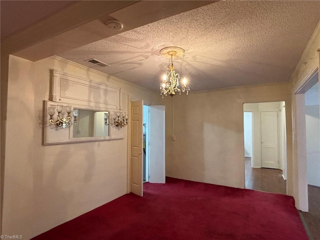 carpeted spare room featuring ornamental molding, a textured ceiling, and a chandelier