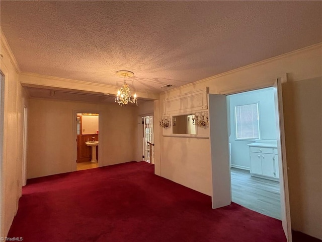 carpeted empty room featuring a textured ceiling, an inviting chandelier, and crown molding