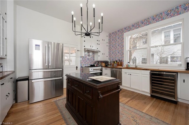 kitchen with wine cooler, light wood finished floors, appliances with stainless steel finishes, a sink, and under cabinet range hood