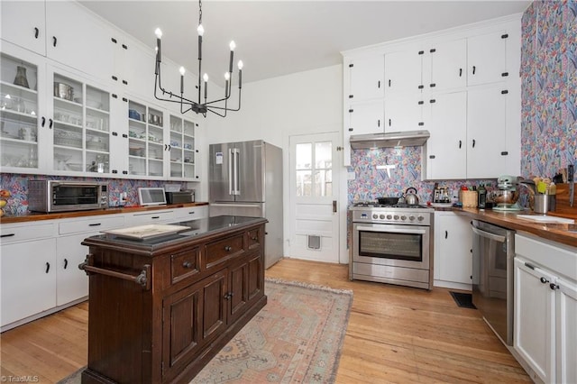 kitchen featuring a toaster, under cabinet range hood, high quality appliances, white cabinets, and light wood-style floors