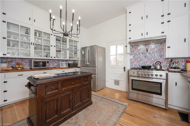 kitchen with stainless steel appliances, dark countertops, decorative backsplash, glass insert cabinets, and under cabinet range hood