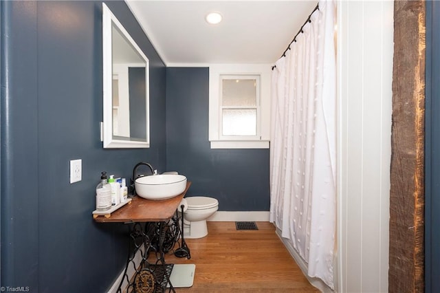 bathroom featuring toilet, wood finished floors, visible vents, a sink, and baseboards