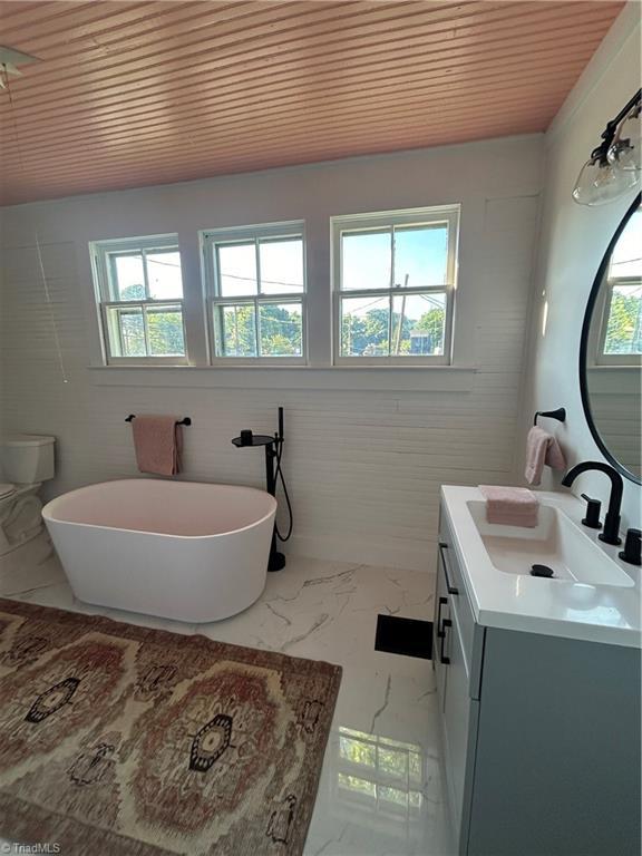 full bathroom with marble finish floor, plenty of natural light, a freestanding bath, and vanity